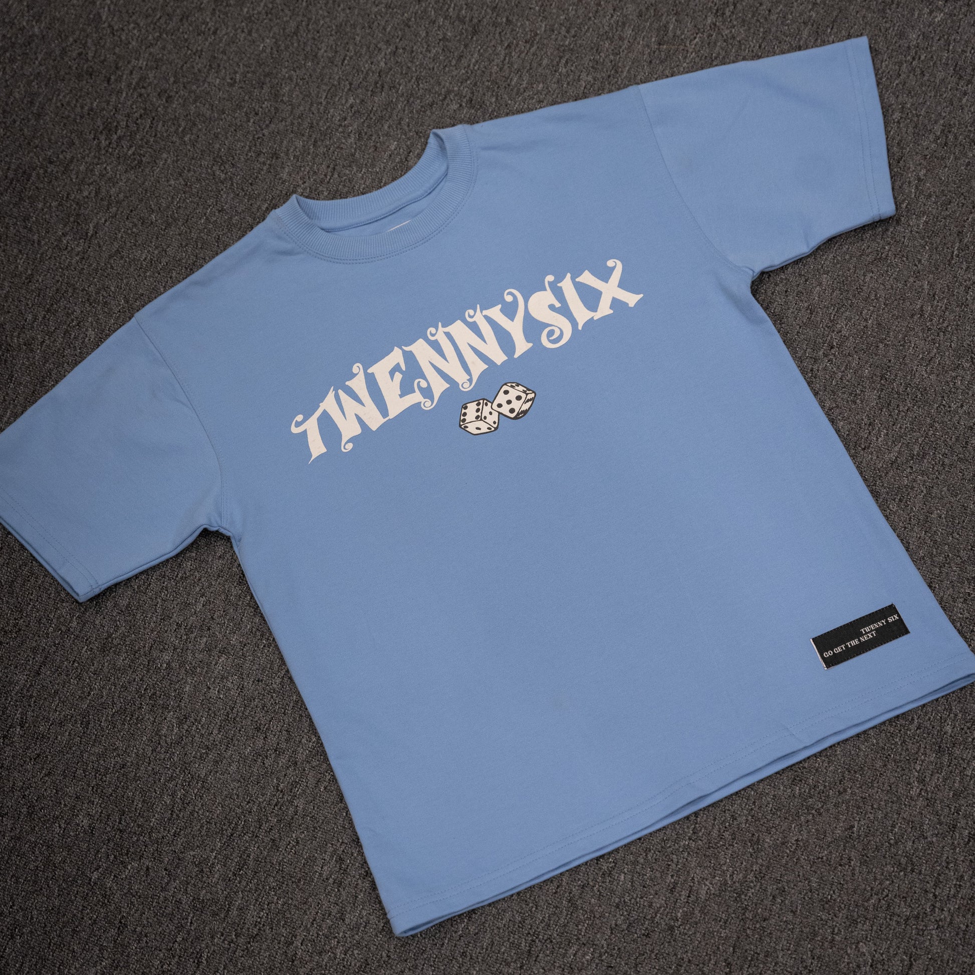 Flat lay image of the Twennysix Dicey T-shirt, showcasing the captivating front design and striking dice puff print in cool blue.