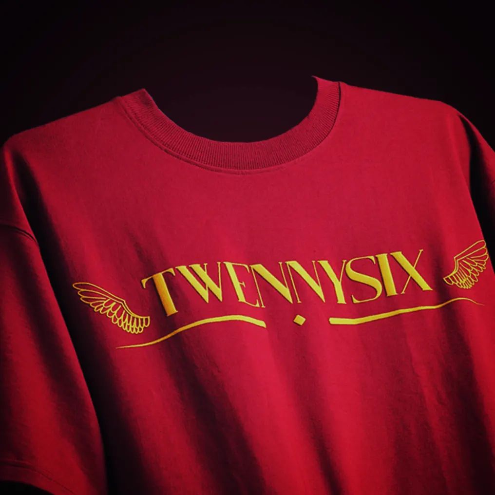 Close-up view of the front branding on the Twennysix Heavenly Hookup T-shirt, featuring the iconic Twennysix emblem with angel wings in vibrant yellow on a maroon background.