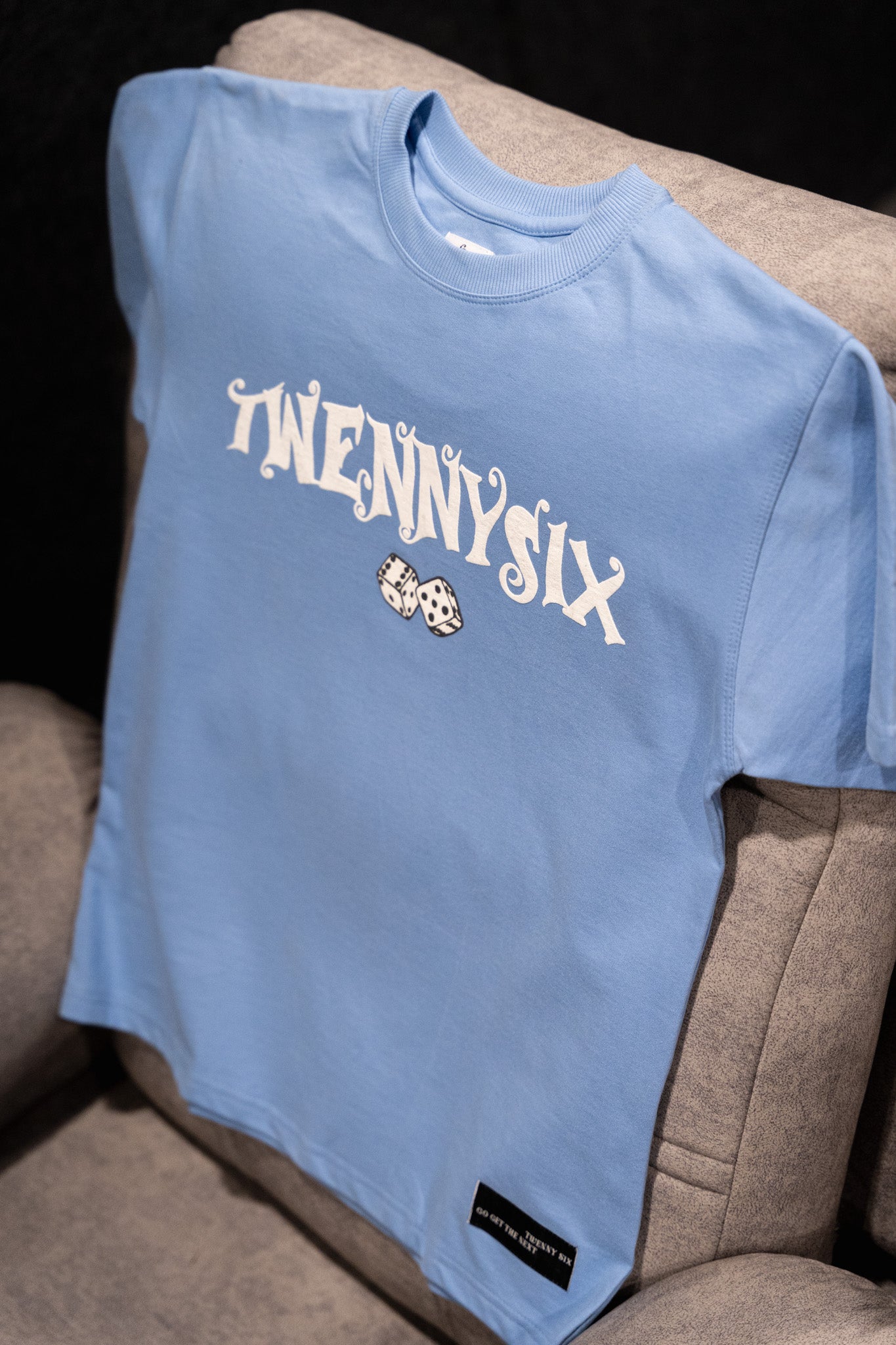 Flat lay image of the Twennysix Dicey T-shirt resting casually on a sofa, showcasing its versatile style and comfort.